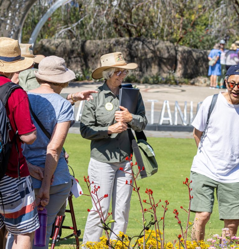 A volunteer guide leads a group of visitors across a lawn at Kings Park