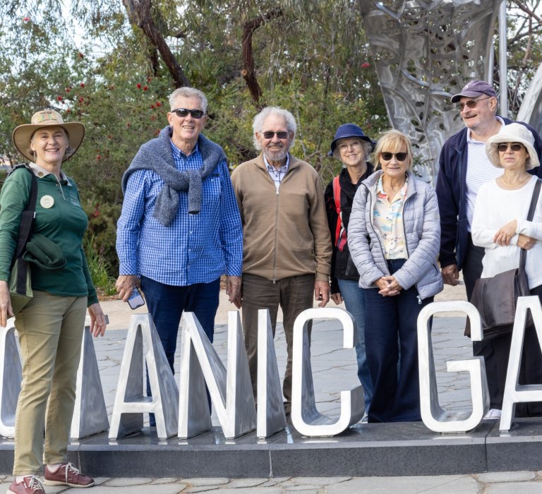 A group of park visitors stand behind the Western Australian Botanic Garden sign at Kings Park